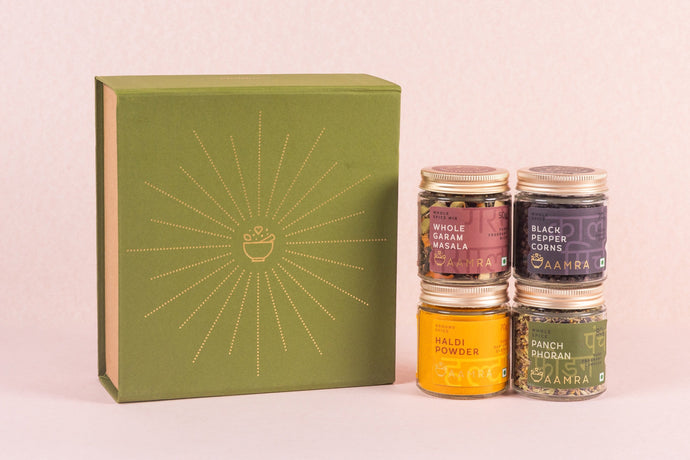 Set of four spice ars with labels in front of a green box on a light pink background