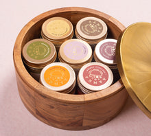Wooden spice box with gold lid containing small containers with brass  on a pink backgroundid