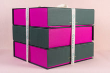 Stack of pink and green boxes with a measuring tape on a pink background