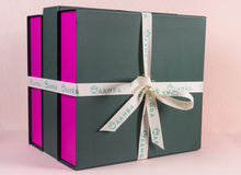 Green gift box with pink accents and a white ribbon on a light pink background